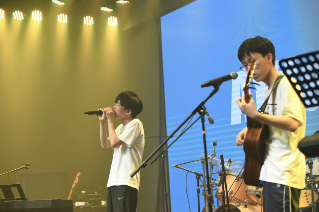 在台上纵声歌唱的杨嘉源和认真弹奏的邹子健.